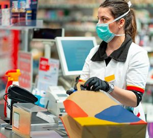 A cashier at the checkout wears a mask and gloves