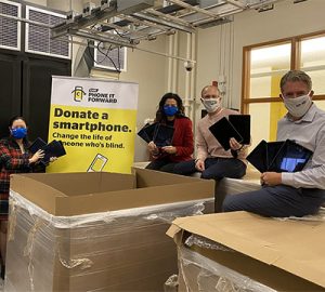 Members from the CNIB and BMO teams stand together beside a large Phone It Forward Banner. In the foreground are boxes full of donated iPads. From left to right, Suzanne Decary, Executive Director, Ontario South for CNIB, Tanya Thung and Rosemary Torelli from BMO Financial Group, Gary Nenson, Vice President, Philanthropy for CNIB and John M. Rafferty, President and CEO for CNIB. Each person holds a few iPads in their arms.