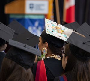 A colourful graduation cap stands out in a sea of black graduation caps